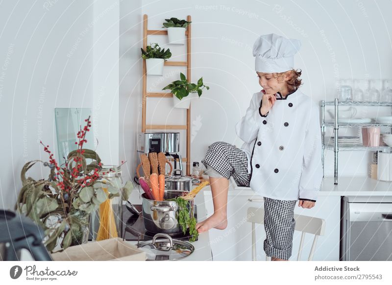 Boy in cook hat with upped hand near pot on chair in kitchen Cook Boy (child) Pot Hand Kitchen Chair chef Child Vegetable Hat Cooking Modern Funny Home Light