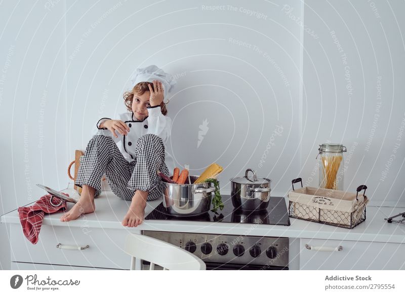 Boy in cook hat sitting near pots on electric fryer in kitchen Cook Boy (child) Pot Kitchen chef Child Vegetable Hat Stove & Oven Cooking Modern Funny Home