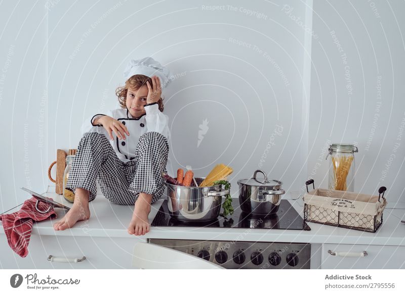 Boy in cook hat sitting near pots on electric fryer in kitchen Cook Boy (child) Pot Kitchen chef Child Vegetable Hat Stove & Oven Cooking Modern Funny Home