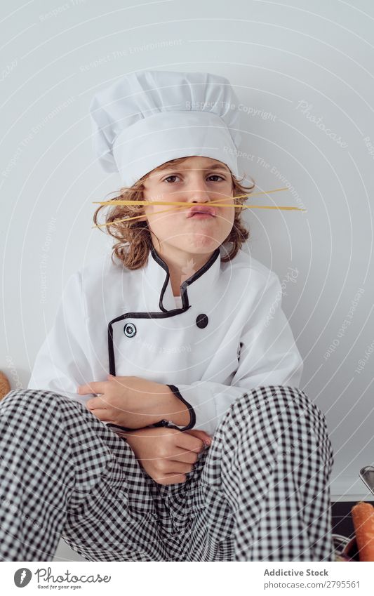 Boy in cook hat making moustache of macaroni in kitchen Cook Boy (child) Kitchen Moustache Macaroni chef Child Hat Pasta Dry Make Cooking Modern Funny Home