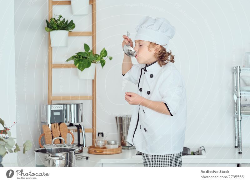 Boy in cook hat holding ladle near mouth in kitchen Cook Boy (child) Kitchen Ladle Mouth chef Child Pot tasting Food Hat Cooking Metal Modern Home Light