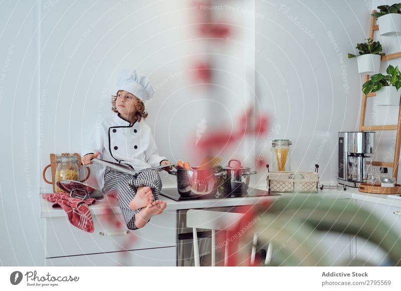 Boy in cook hat with book sitting near pots on electric fryer in kitchen Cook Boy (child) Book Pot Kitchen chef Child Vegetable Hat Volume Reading Stove & Oven