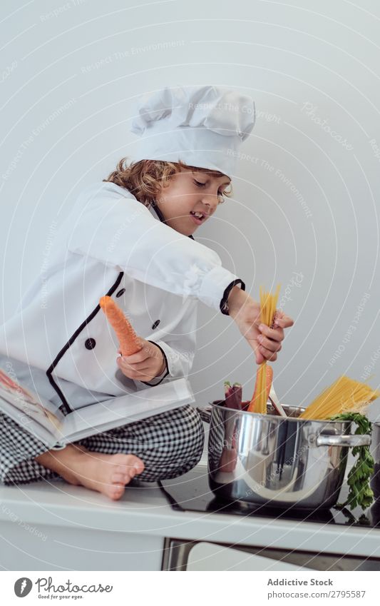 Boy in cook hat putting pasta in pot on electric fryer in kitchen Cook Boy (child) Pot Pasta Kitchen chef Child Macaroni Carrot Vegetable Hat Stove & Oven Putt