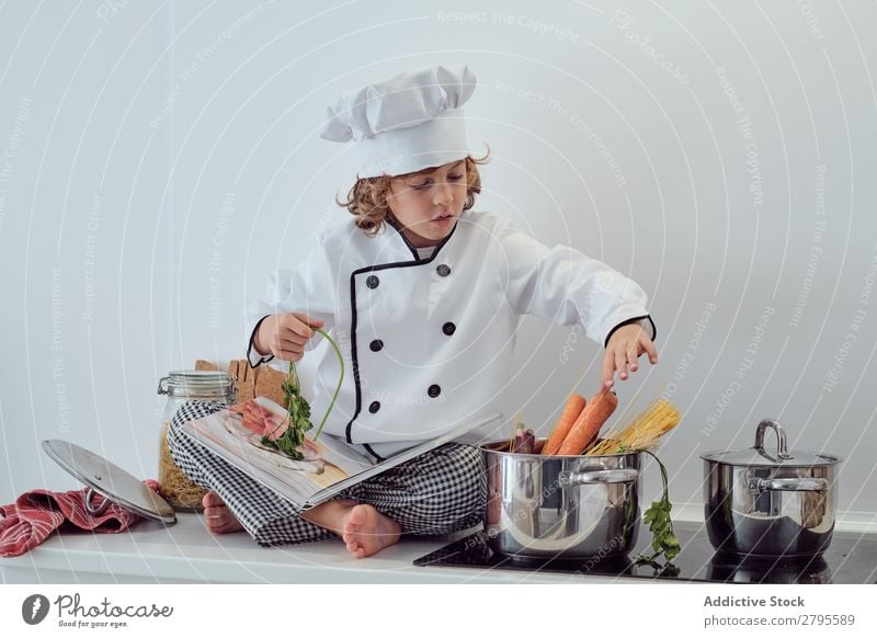 Boy in cook hat putting pasta in pot on electric fryer in kitchen Cook Boy (child) Pot Pasta Kitchen chef Child Macaroni Carrot Vegetable Hat Stove & Oven Putt