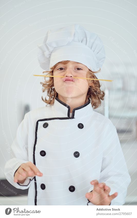 Boy in cook hat making moustache of macaroni in kitchen Cook Boy (child) Kitchen Moustache Macaroni chef Child Hat Pasta Dry Make Cooking Modern Funny Home