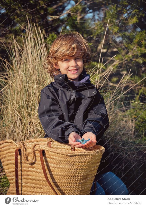 Boy with heap of garbage in hands near basket Trash container picking up Ground Child Park litter picker Boy (child) Container cleaning up Environment Plastic