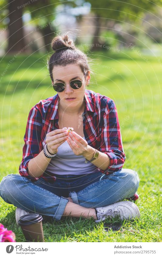 Front view of a young hipster woman sitting on grass in a park while holding a flower in a sunny day Young woman Hipster Hip & trendy Sit Hold Flower Park Grass
