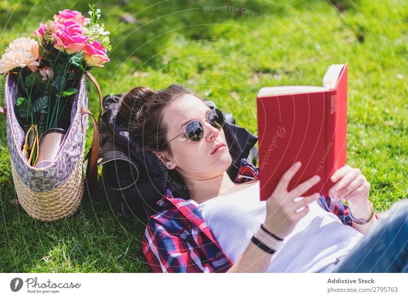 Side view of a hipster happy woman lying on grass in sunny day at park while reading a red book Profile Young woman Hipster Hip & trendy Lie (Untruth) Reading