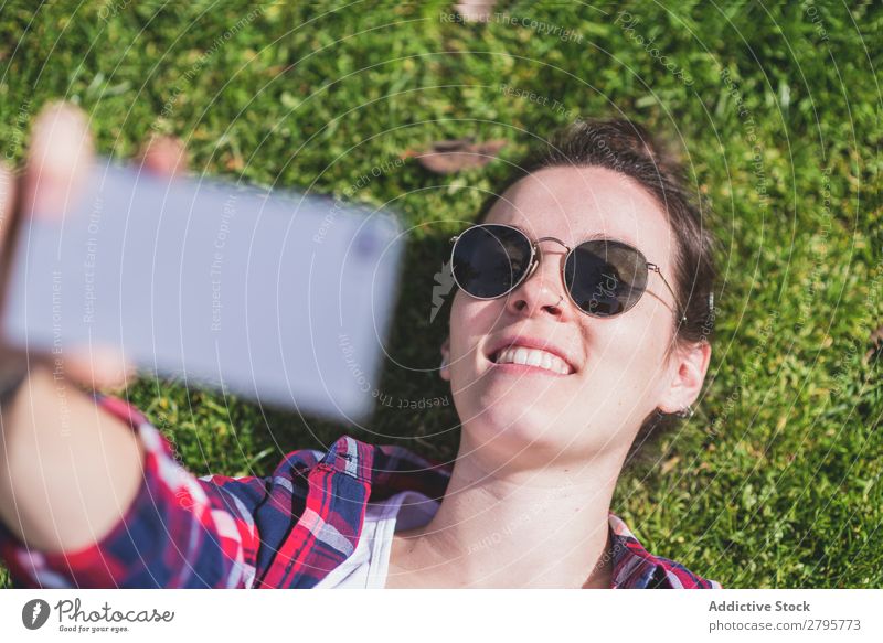 Above view of a young smiling hipster woman lying on grass in a sunny day at a park while taking a selfie with a mobile phone Young woman Hipster Hip & trendy