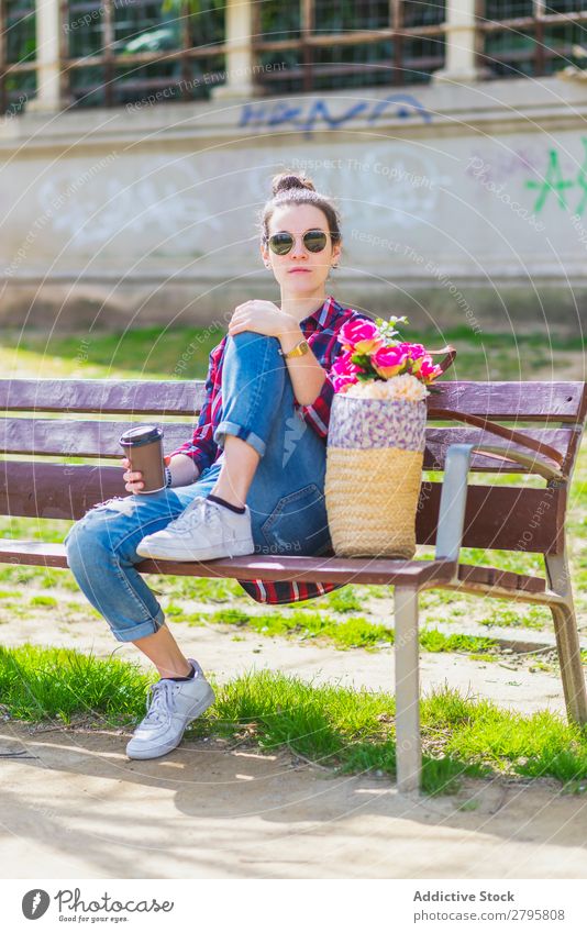 Front view of a young hipster woman sitting on a park bench relaxing in a sunny day while looking to camera Young woman Hipster Hip & trendy Sit looking camera