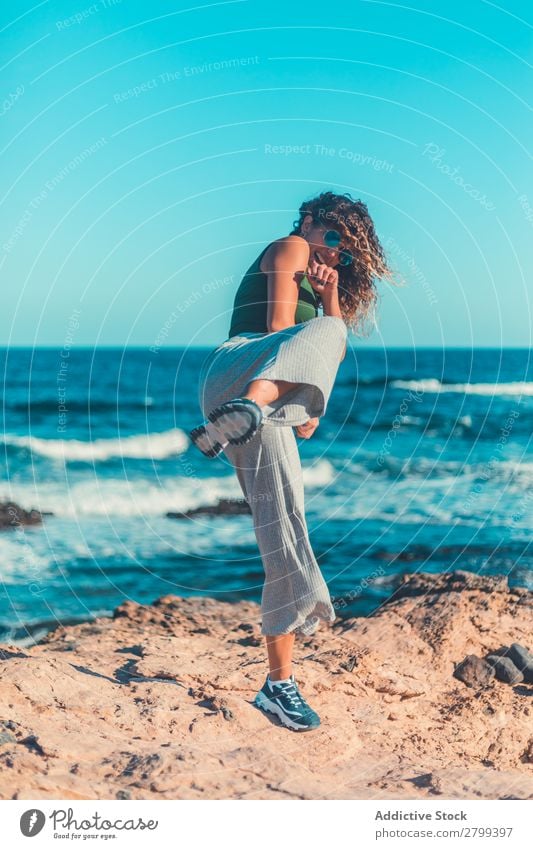 Anonymous female kicking air on seashore Woman Ocean Coast Sky Blue Beautiful weather Lifestyle Leisure and hobbies Waves Stone Water Movement Practice Balance