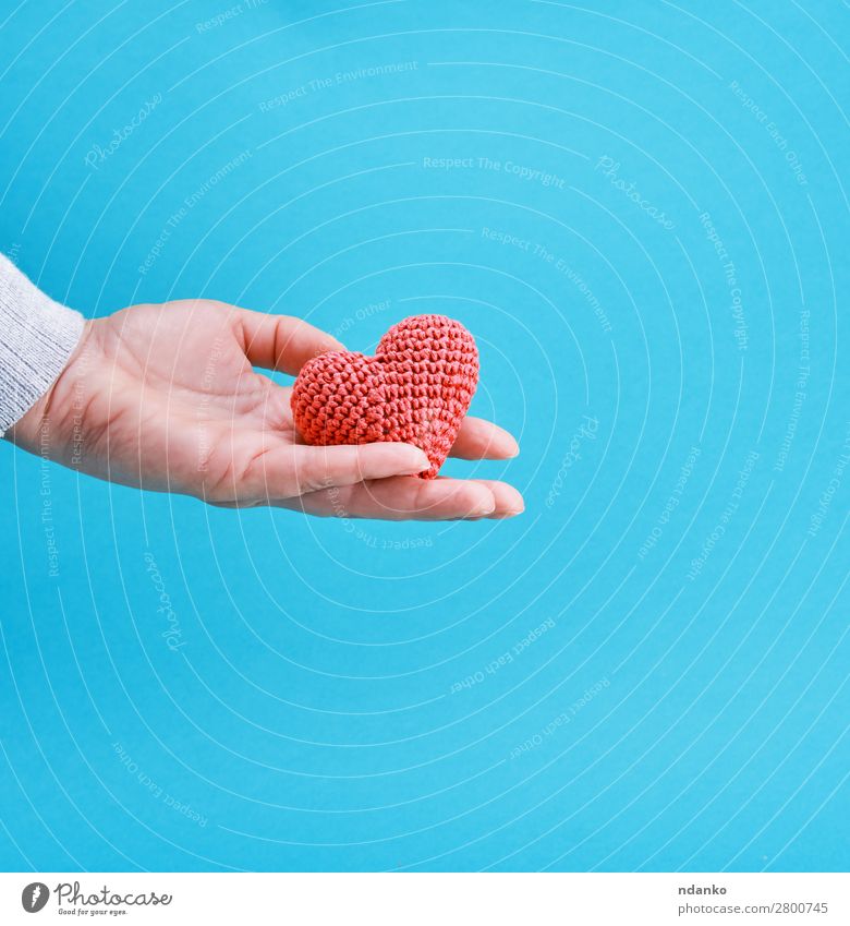 small knitted red heart in a human hand Decoration Feasts & Celebrations Valentine's Day Wedding Hand Heart Love Blue Red Romance Colour Hope Idea background