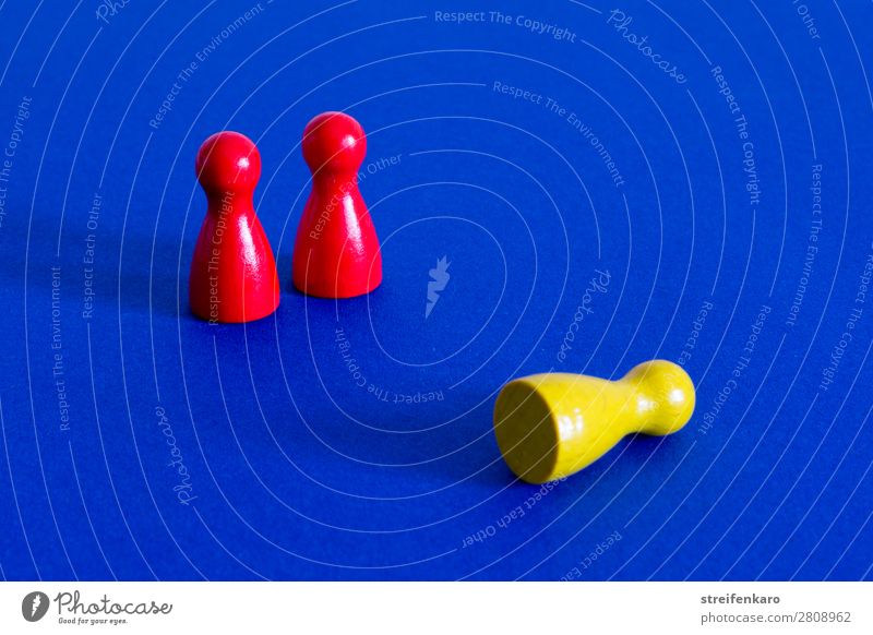 A yellow playing piece lies in front of two standing red playing pieces on a blue background Economy Business Company Success Team Toys Wood To fall Hunting