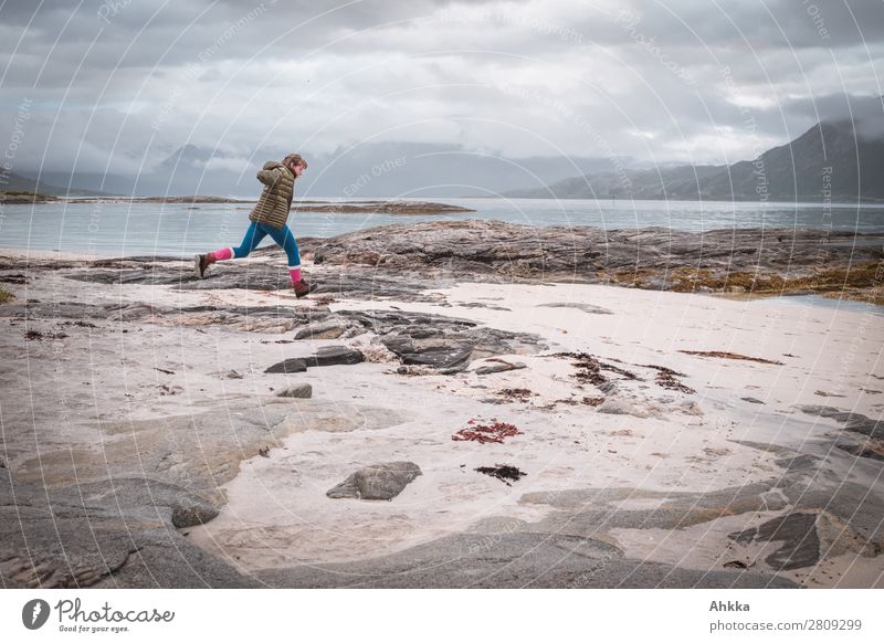 Young woman jumps on the beach in front of a Norwegian coastal panorama Vacation & Travel Adventure Far-off places Freedom Island Youth (Young adults) Nature