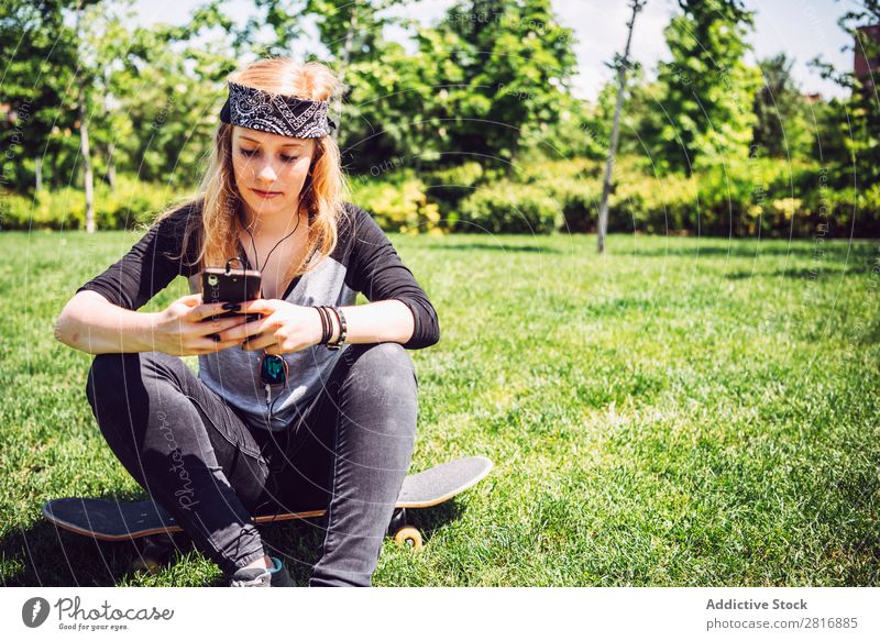 Woman skateboarder listening music from smart phone in a park Music Headphones Joy Park PDA Listening Chinese Culture Cellphone Exterior shot Young woman Sit