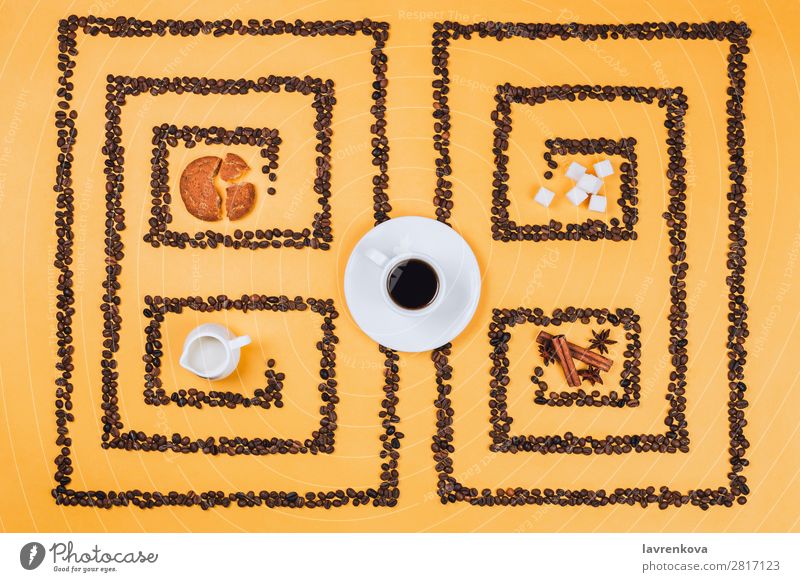 Flatlay of coffee cup in the middle of pattern or labyrinth made of coffee beans with cookies, milker, spices and sugar Cinnamon anise stars Herbs and spices