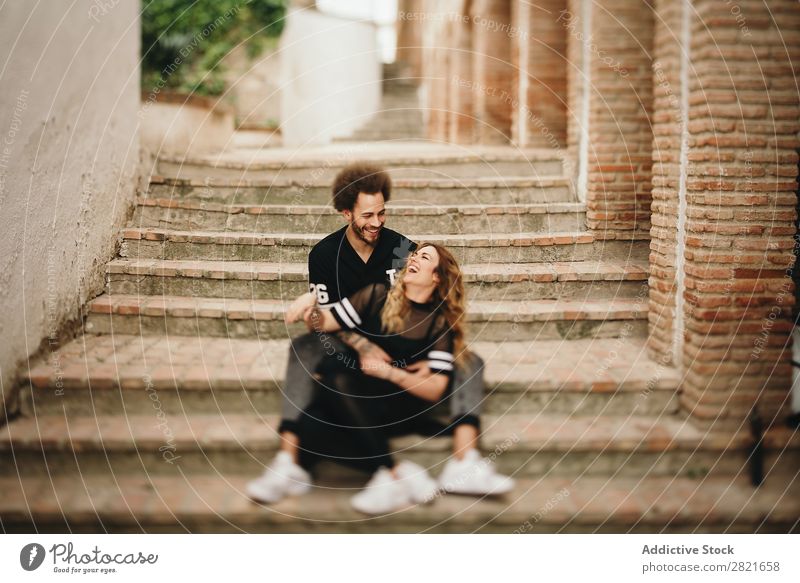 Couple laughing while hugging on steps in city Laughter having fun Portrait photograph Street Sit Together Embrace Steps Rural Stairs Cheerful candid Happy