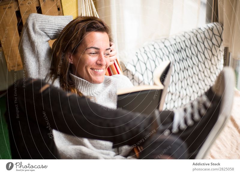 Cheerful woman lying with book Woman Home Relaxation Lie (Untruth) Hammock Reading Smiling Book Literature Lifestyle Beautiful Room Human being Easygoing Adults