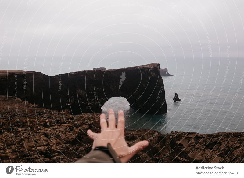 Crop hand outstretched to ocean Man Rock Ocean Iceland Hand Height Outstretched Landscape Vantage point Coast Gloomy scenery Extreme seaside Adventure Nature