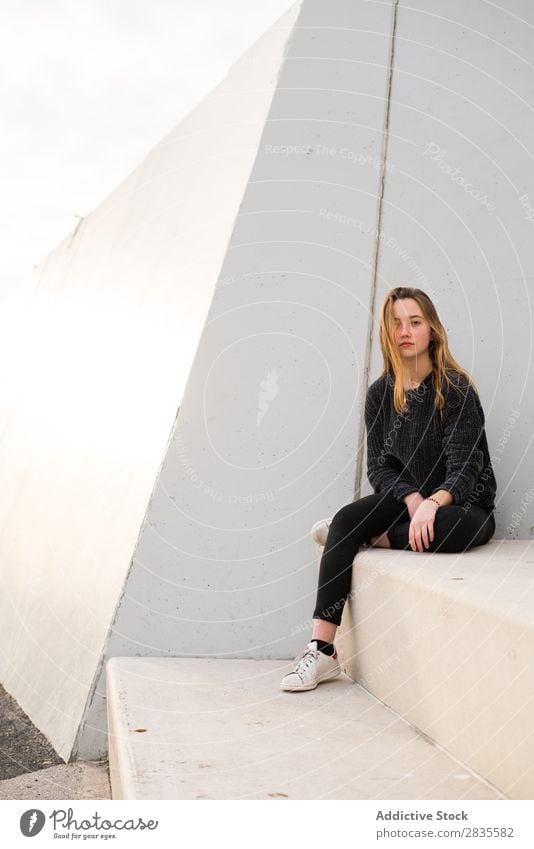 Outdoors portrait of young girl on concrete stairs looking at camera. woman sitting block building dreamy thoughtful pensive pretty beautiful female sweater