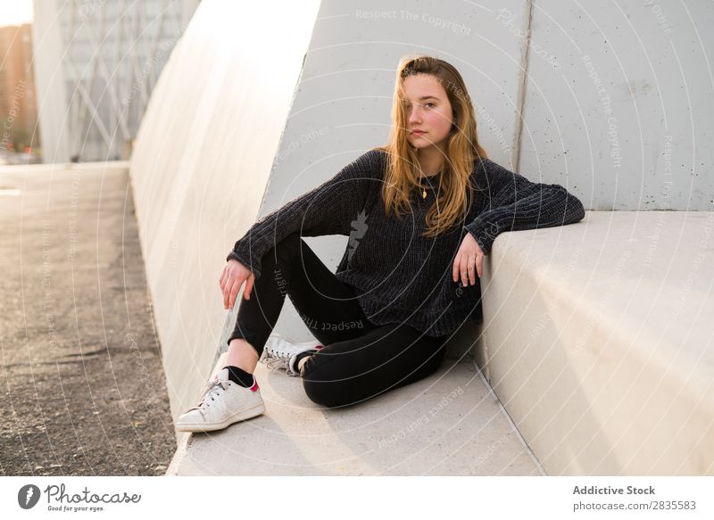 Outdoors portrait of young girl on concrete stairs looking at camera. woman sitting block building dreamy thoughtful pensive pretty beautiful female sweater