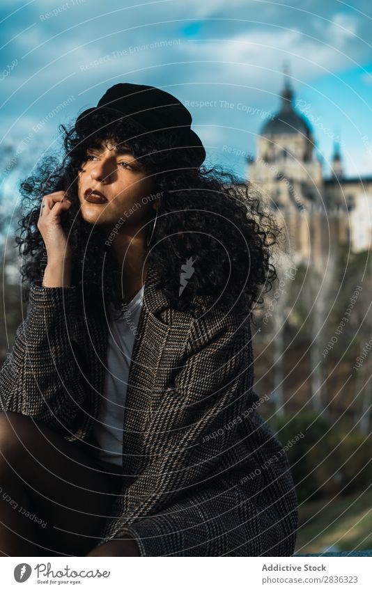 Young stylish woman sitting in city Woman Attractive City fashionable Curly Brunette Coat Hat Sit Fence Vantage point Fashion Youth (Young adults) Beautiful