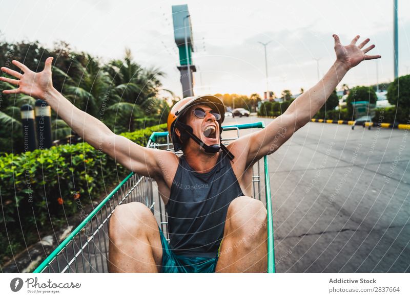 Emotional man in shopping cart Man Shopping Trolley riding Cart pushcart Sunglasses shopper Ride handsome Cheerful Joy Parking lot Human being Markets Humor