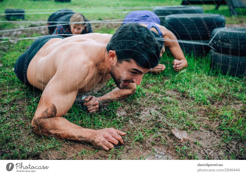 Man in obstacle course crawling under electrified cables Joy Happy Sports Success Human being Woman Adults Group Authentic Dirty Effort Competition Mud