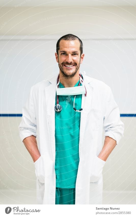 Smiling handsome doctor at hospital. Standing. Arm Background picture Considerate Caucasian Cheerful clinician Doctor Equipment Friendliness Happy Healthy