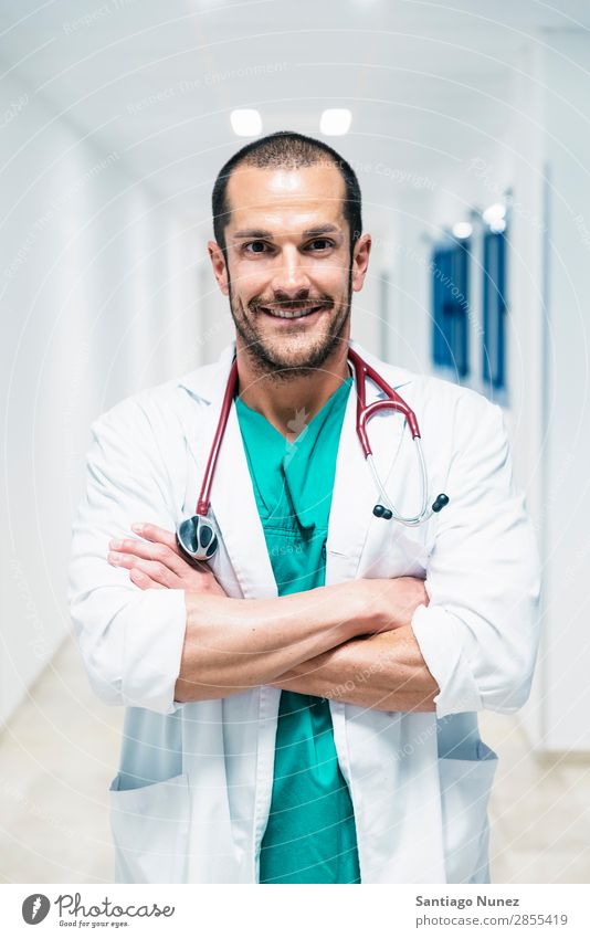 Smiling handsome doctor at hospital. Standing. Arm Background picture Beautiful Considerate Caucasian Cheerful clinic clinician Doctor Equipment Friendliness