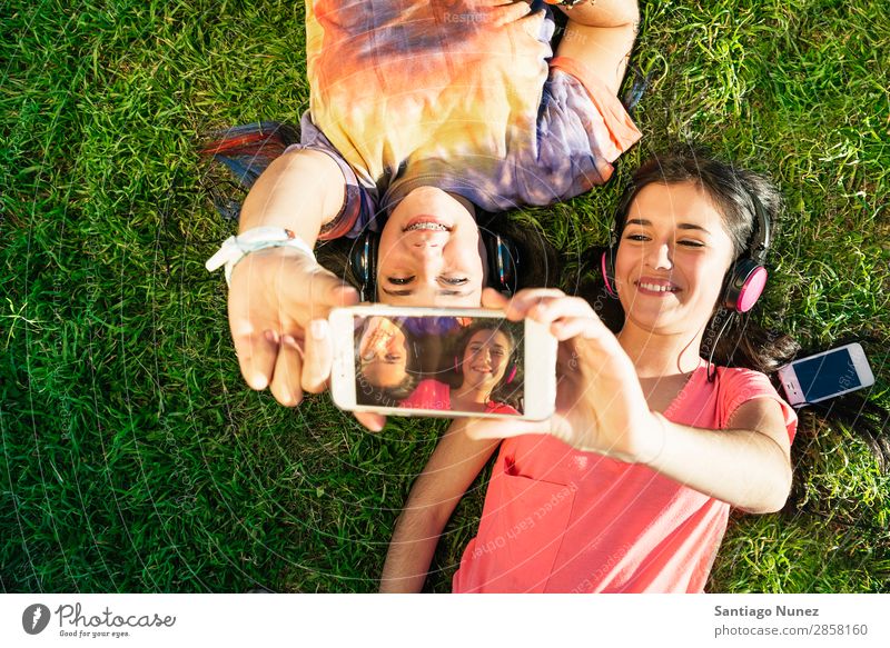Two Teenage Girls Taking Selfie In Park American Attractive Beautiful braket Caucasian Solar cell Cellphone Woman Friendship Joy Grass Happy Headphones Laughter