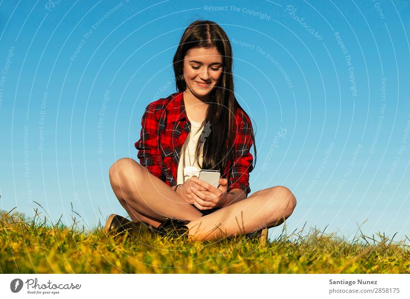Happy Teenage Girl Using Mobile In Park American Attractive Beautiful braket Caucasian Solar cell Cellphone comunication Woman Friendship Joy Grass Headphones