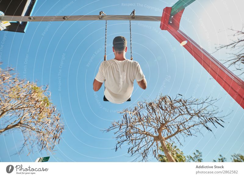 Man swinging on playground in sunlight swings Leisure and hobbies Town Playground Bright Sunlight Blue sky Contentment Street Action Expression Playing
