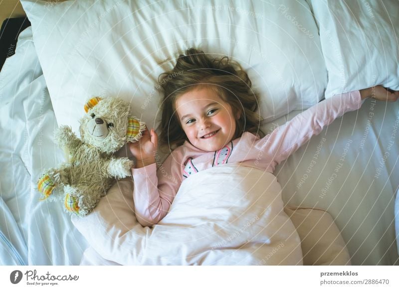 Little girl lying in a bed with teddy bear at the morning. Happy