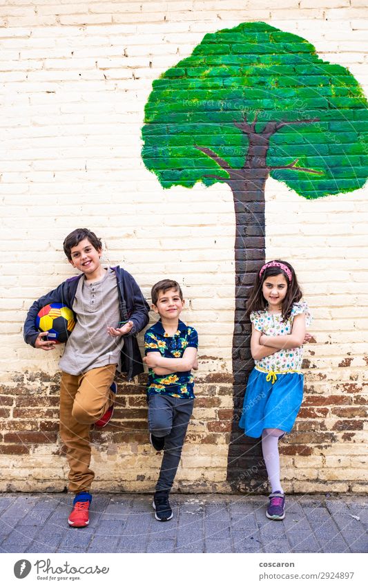 Portrait of three kids with a painted tree background Lifestyle Joy Happy Beautiful Playing Summer Sports Soccer Ball Child School Schoolyard Masculine Feminine