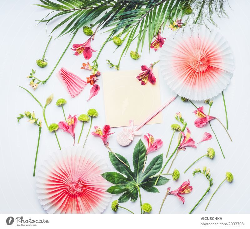 Blank greeting card mock up with paper party fans, tropical leaves and exotic flowers on white background, top view. Flat lay. Frame. Copy space for your text or design