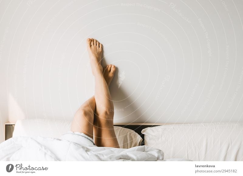 Woman with vitiligo holding pillow between legs on bed in front of white  wall at home