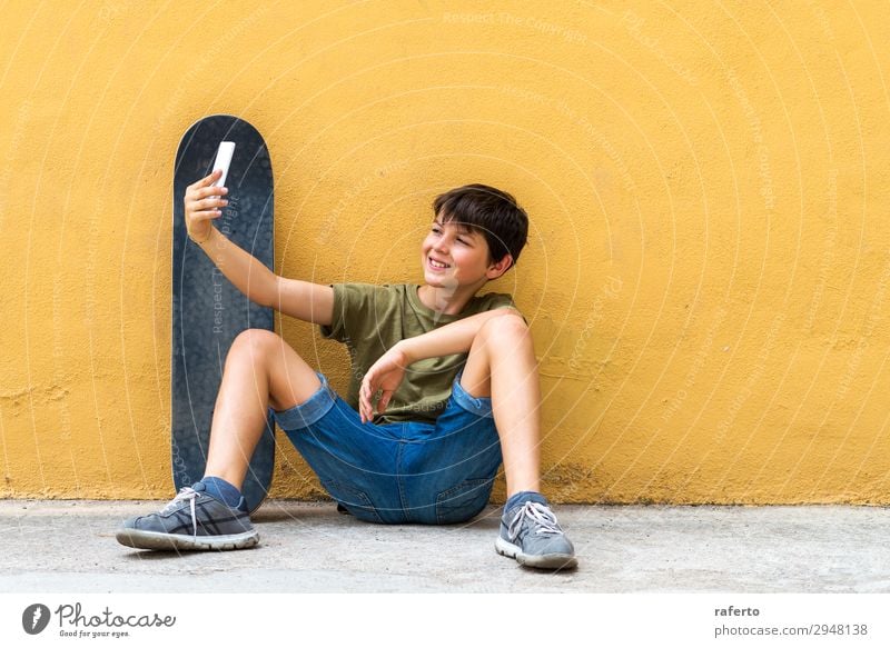 boy sitting on ground leaning on a wall, taking a selfie Happy Child Telephone PDA Technology Human being Boy (child) Youth (Young adults) 1 13 - 18 years