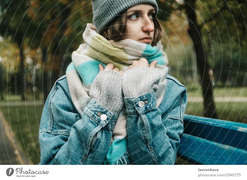 young adult woman sitting on a bench wrapped in scarf Loneliness Tree Bench Hat Denim Cold Exterior shot Model hair Adults Attractive Hipster Lifestyle White