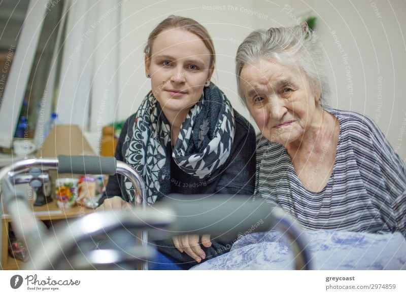 A portrait of a young fair haired woman sitting close to the elderly lady whose hand is on her arm. Both of them are slightly smiling Human being Feminine