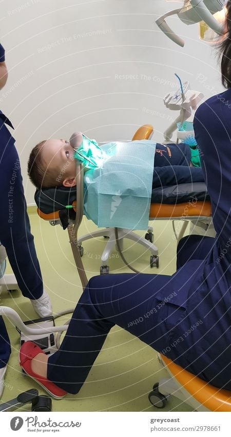 A fragment of a dental room with a kid, lying on a dental chair, and a part of his doctors figure Medical treatment Child Work and employment Doctor Human being