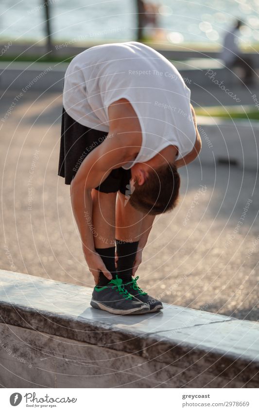 A teenage boy stretches down, pulling his head to his knees, outdoors Sports Track and Field Sportsperson Yoga Masculine Young man Youth (Young adults) 1