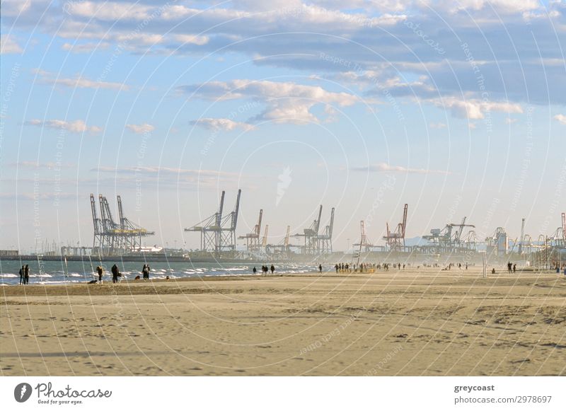 People walking on the beach of Valencia in winter, Spain. Scene with industrial port and container cranes Beach Ocean Industry Sky Waves Coast Inland navigation