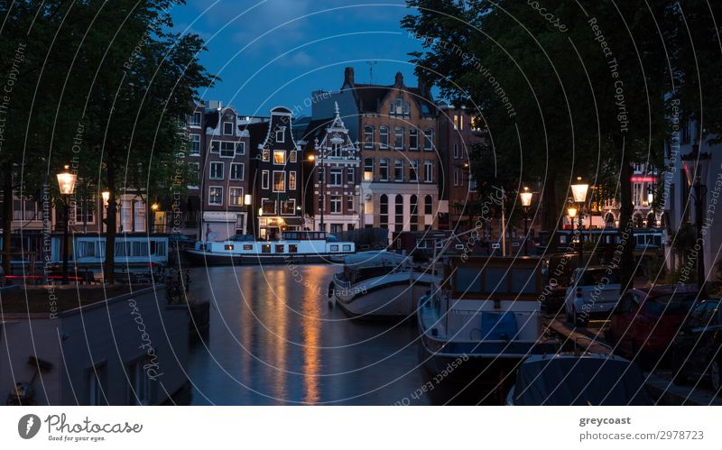 Amsterdam night scene with traditional houses, boats moored along the canal and lit lanterns, Netherlands Vacation & Travel Tourism Sightseeing