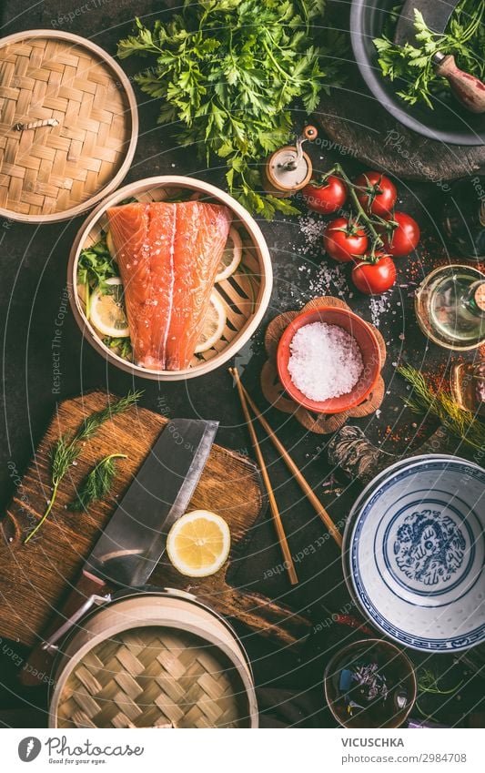 Authentic asian food cooking preparation with salmon,seasoning, spices, bowls and chopsticks on dark kitchen table, top view. Various ingredients, utensils and tools on kitchen table.  Asian cuisine