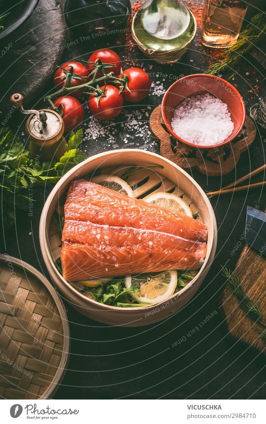 Raw salmon fillet in bamboo steamer on dark rustic kitchen table with fresh ingredients and tools. Healthy eating and cooking. Dieting concept. Asian cuisine. Cooking preparation