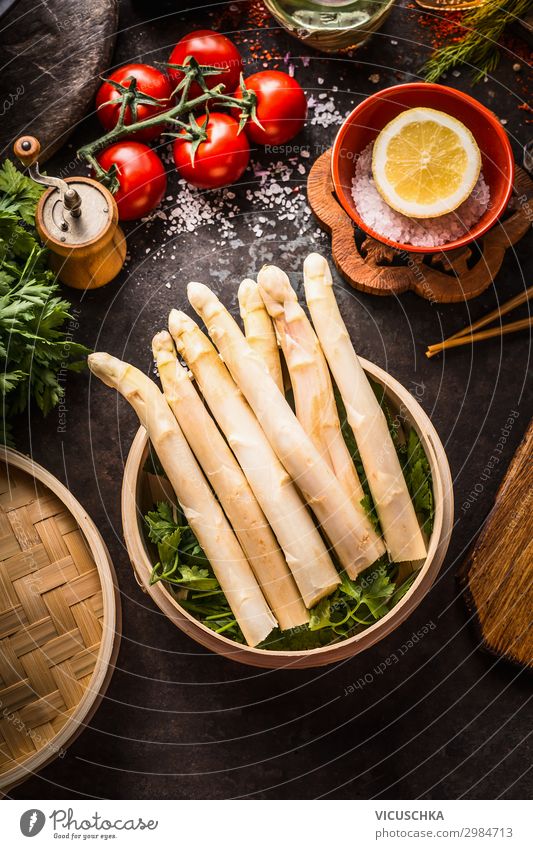Asparagus in bamboo steamer on dark rustic kitchen table with ingredients and chopsticks, top view. Healthy eating and seasonal cooking. Asian food. asparagus