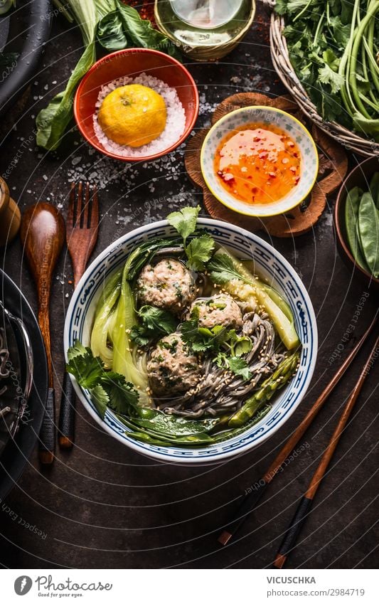 Asian noodles bowl with green vegetables, bok choy and meat balls on dark background with wooden cutlery, chopsticks and hot sauce, top view. Close up. Healthy asian meal. Asian cuisine concept