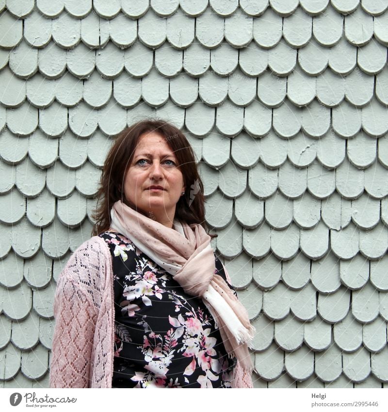Woman with dark long hair, colourful dress, pink cardigan and pink scarf is standing in front of a grey wall of wooden shingles Human being Feminine Adults 1