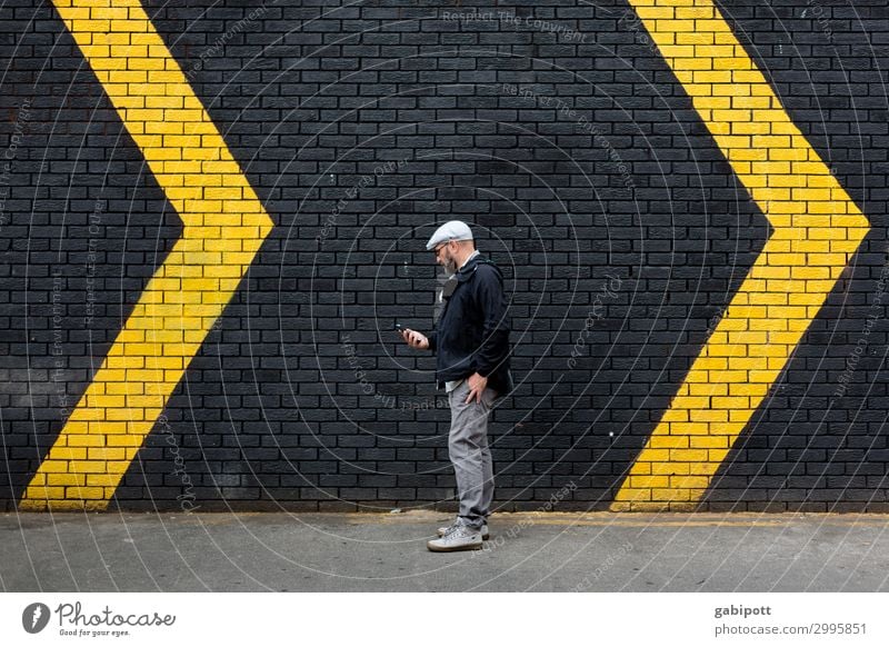 Man in front of a black wall with yellow arrows Human being Masculine Adults 1 Wall (barrier) Wall (building) Facade Sign Signs and labeling Signage